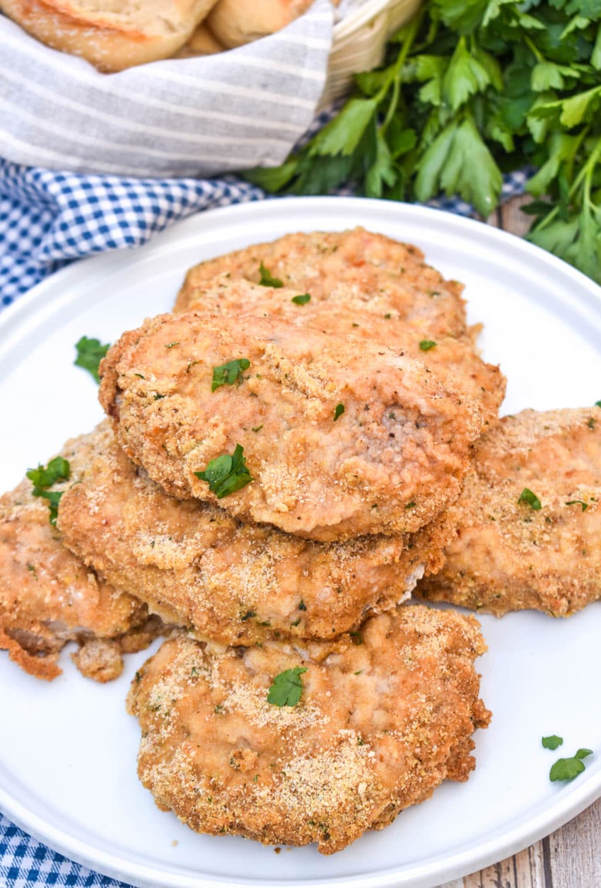 breaded ranch pork chops with ranch dressing stacked on a white serving plate