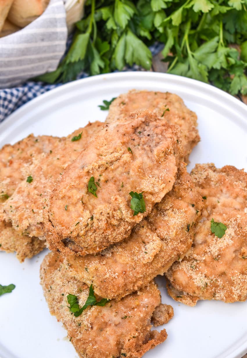breaded ranch pork chops with ranch dressing stacked on a white serving plate