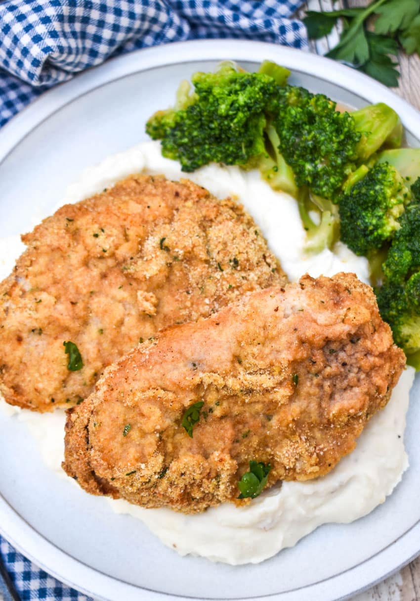breaded pork chops with ranch dressing over mashed potatoes on a white plate with steamed broccoli on the side