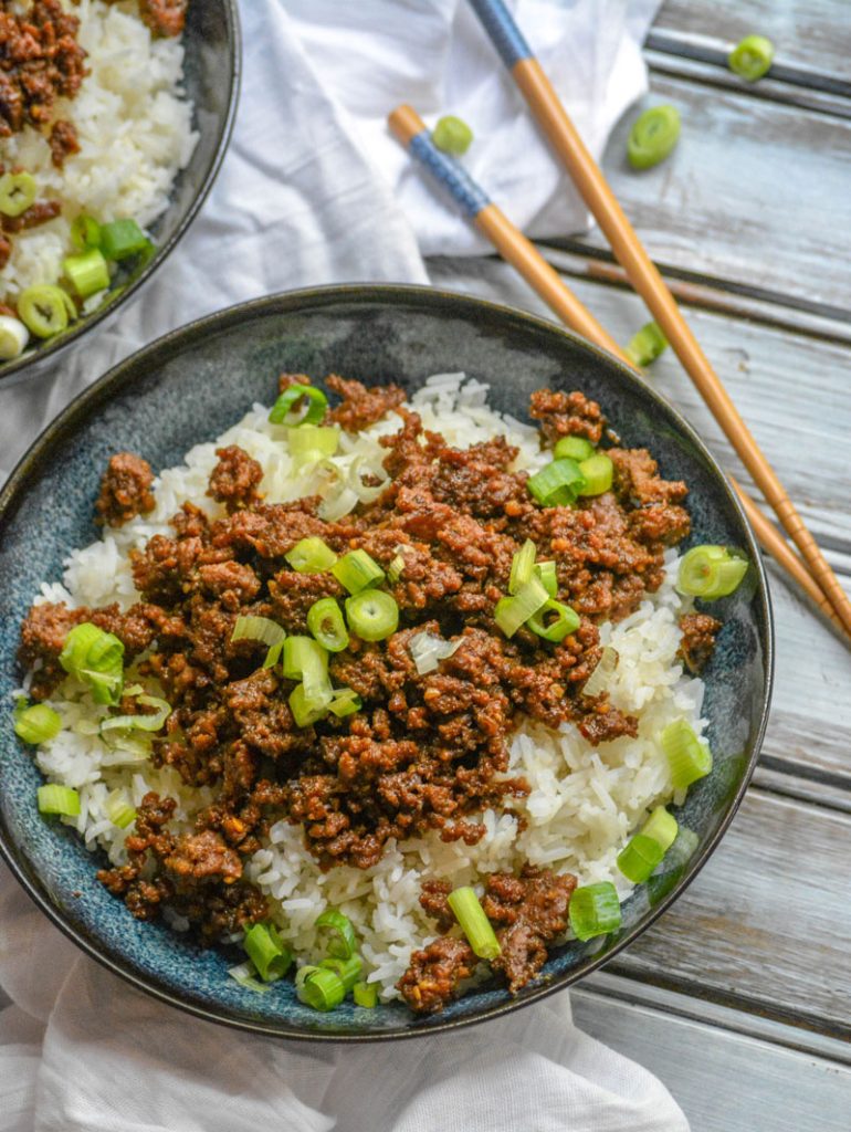 Korean Barbecued Beef with sliced green onions over steamed white rice in blue bowls