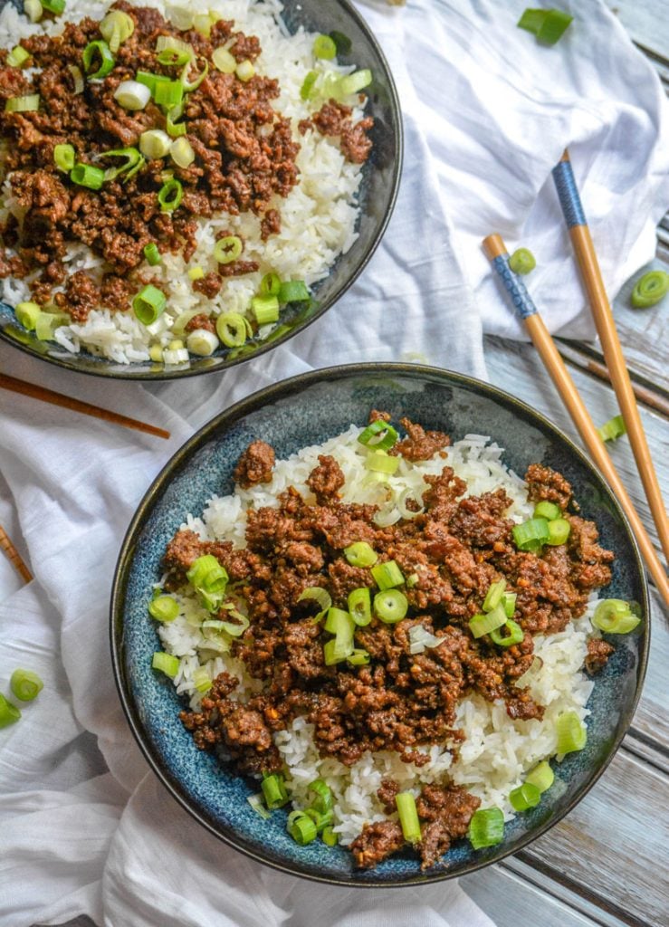 Korean Beef with sliced green onions over steamed white rice in blue bowls