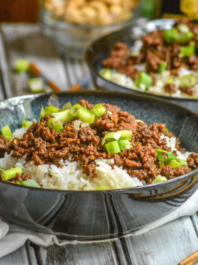 Korean Beef with sliced green onions over steamed white rice in blue bowls