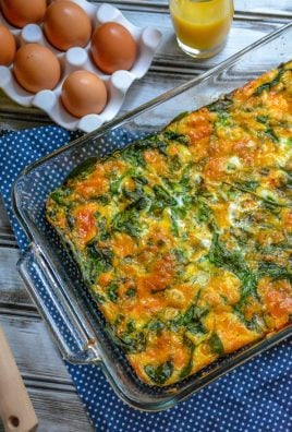 spinach and cheddar egg bake in a glass 9x13 baking dish with fresh eggs and a glass of orange juice in the background