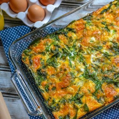 spinach and cheddar egg bake in a glass 9x13 baking dish with fresh eggs and a glass of orange juice in the background