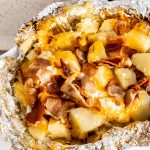 a foil packet torn open to reveal grilled potatoes covered in a blend of melted cheeses