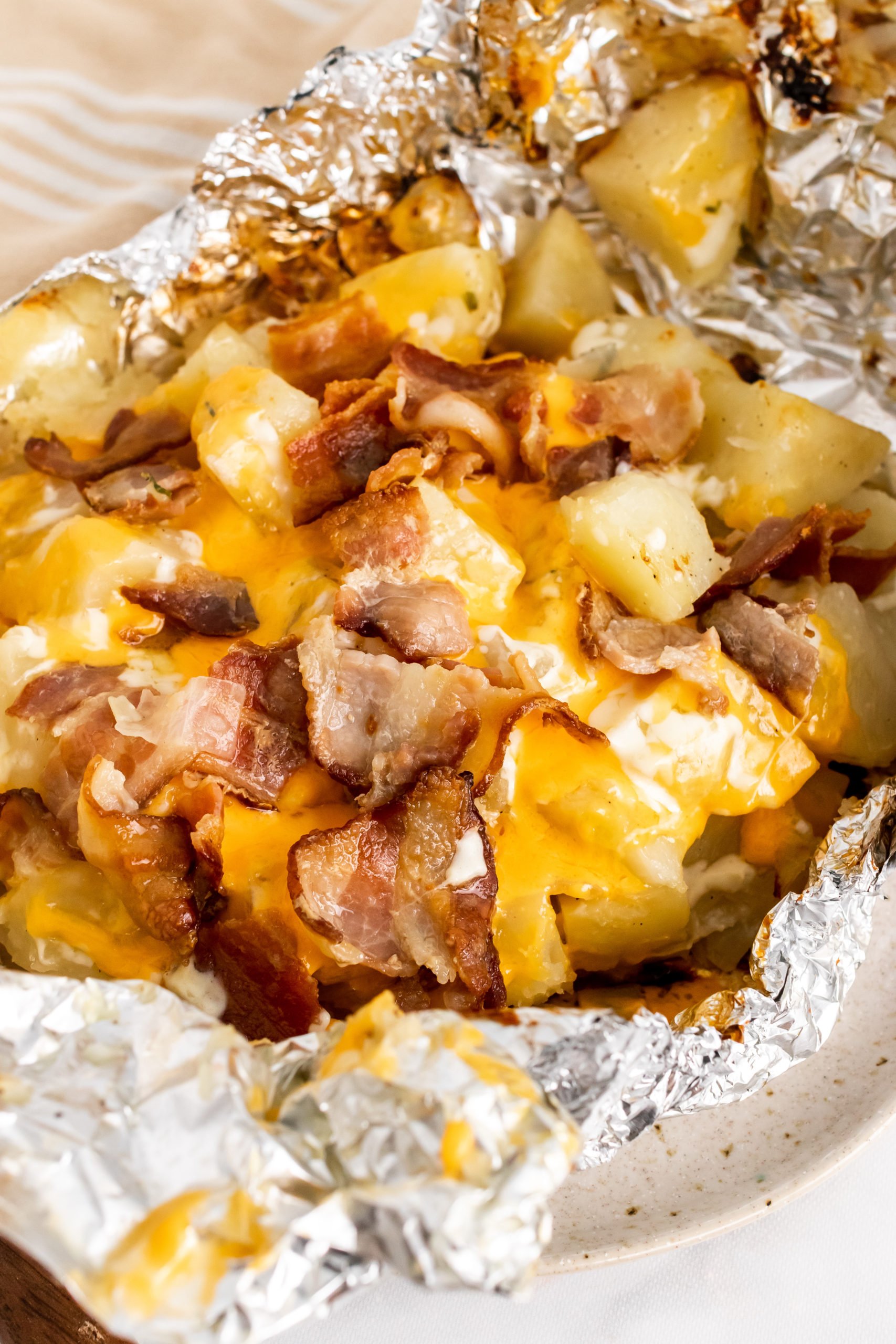 a foil packet torn open to reveal grilled potatoes covered in a blend of melted cheeses