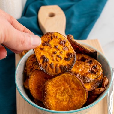 a hand holding up a chip from a bowl of honey cinnamon seasoned sweet potato chips