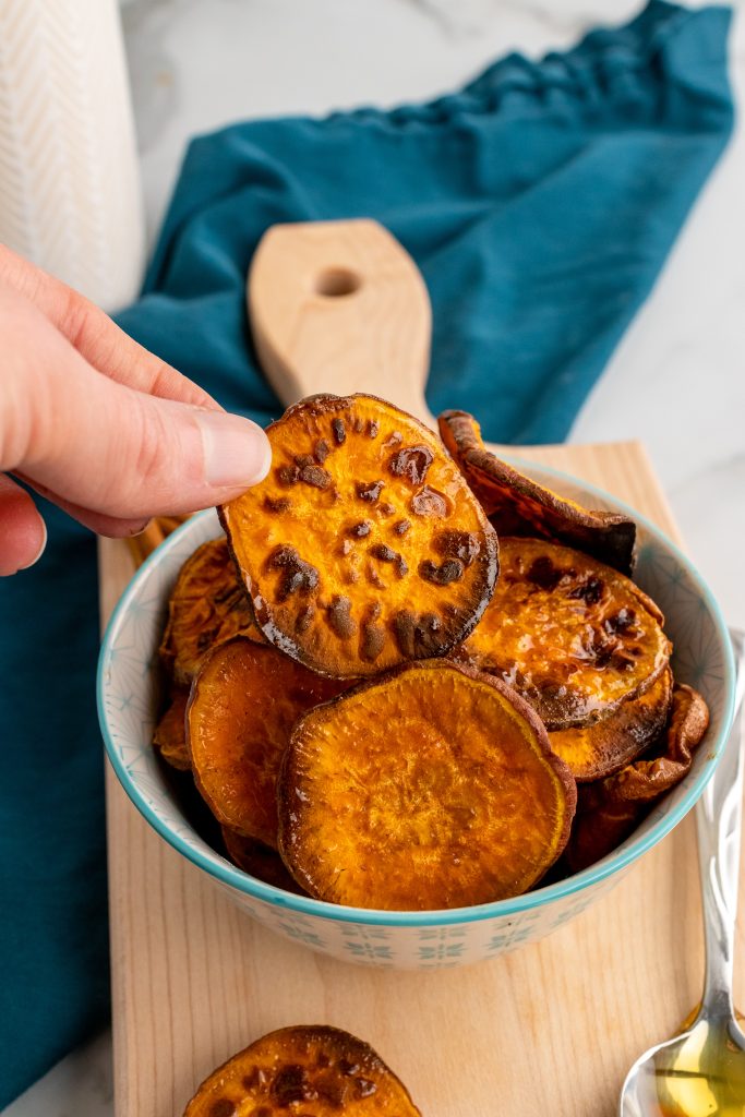 a hand holding up a chip from a bowl of honey cinnamon seasoned sweet potato chips