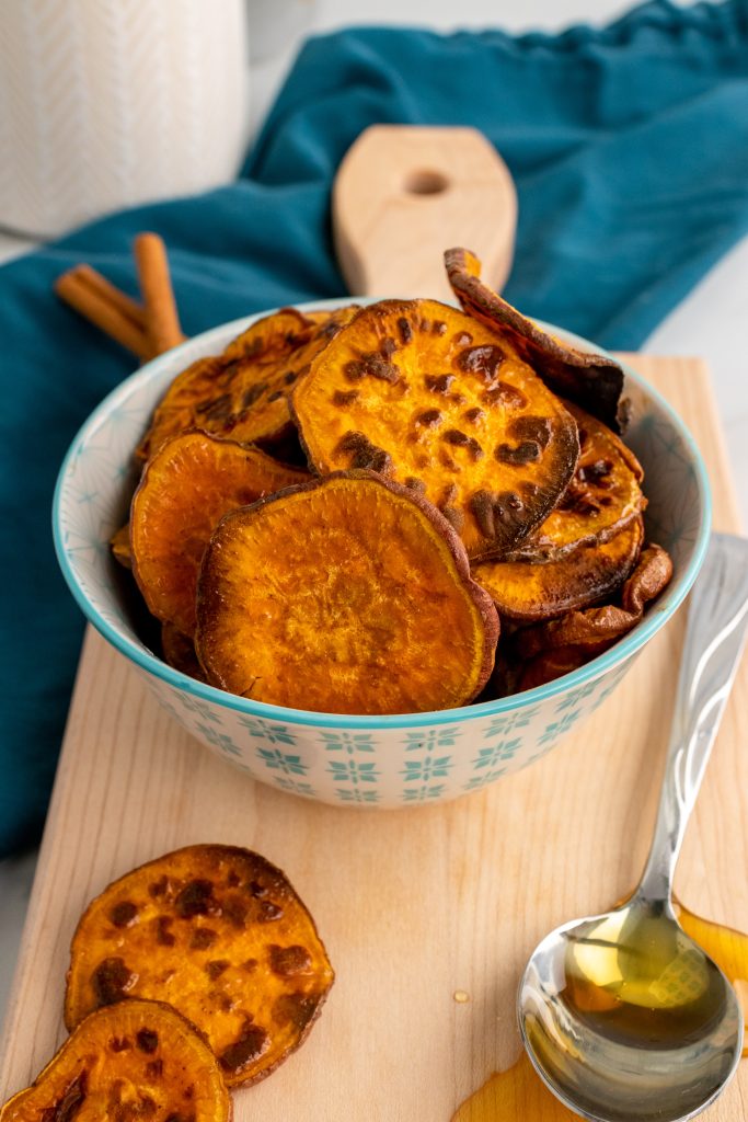 crispy sweet potato chips in a blue and white bowl on a wooden cutting board