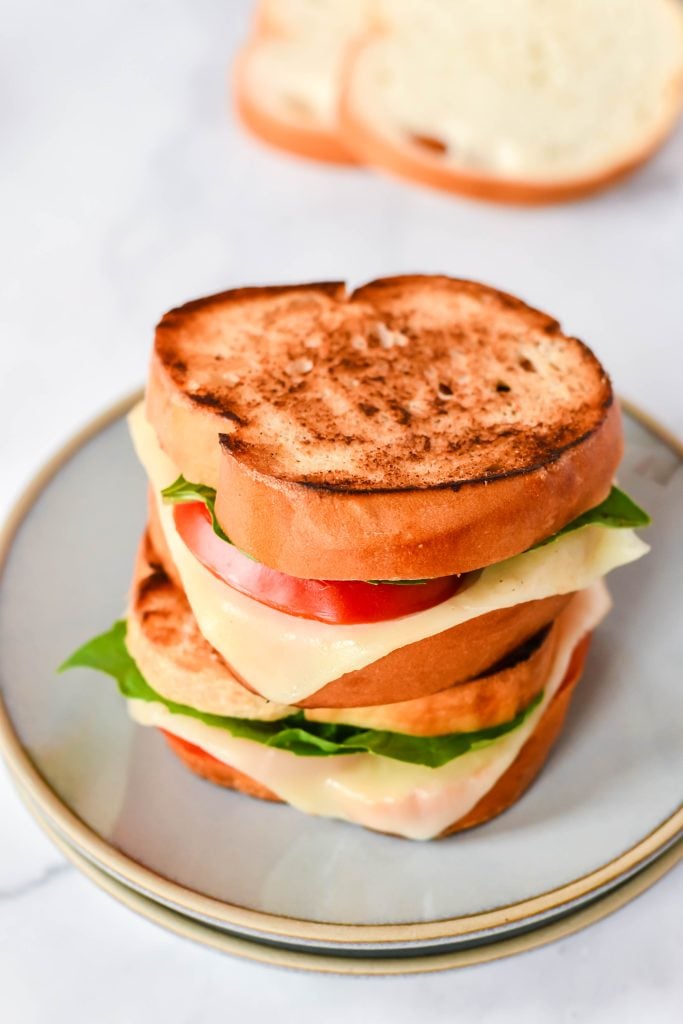 caprese grilled cheese on a stack of gray lunch plates with sliced bread in the background