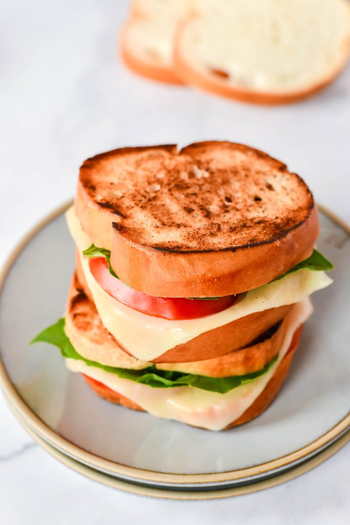 caprese grilled cheese on a stack of gray lunch plates with sliced bread in the background