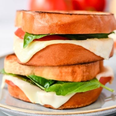 caprese grilled cheese on a stack of gray lunch plates with vine ripened tomatoes in the background