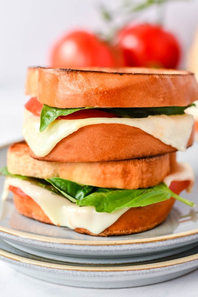 caprese grilled cheese on a stack of gray lunch plates with vine ripened tomatoes in the background