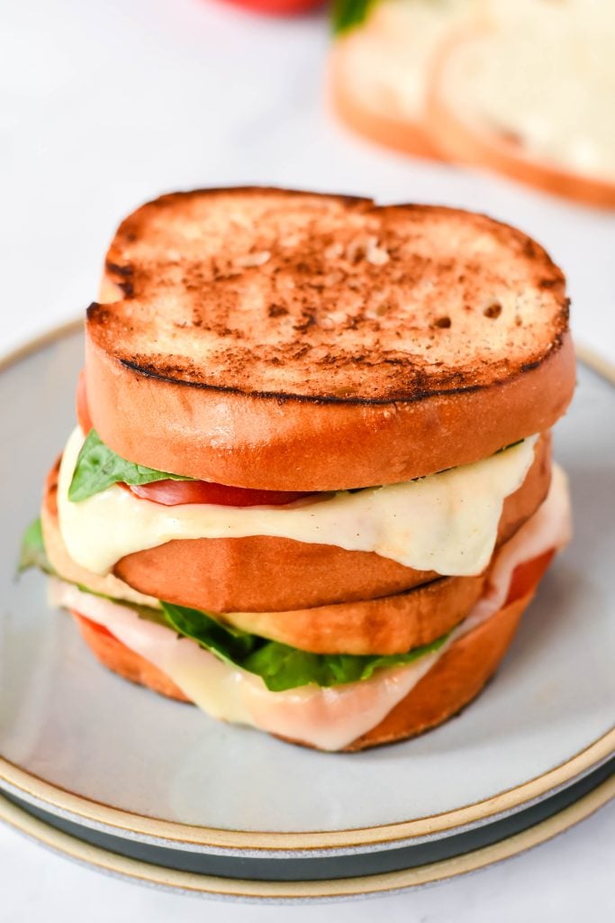 caprese grilled cheese on a stack of gray lunch plates with vine ripened tomatoes in the background