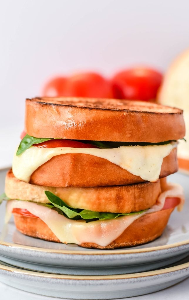 caprese grilled cheese on a stack of gray lunch plates with vine ripened tomatoes in the background