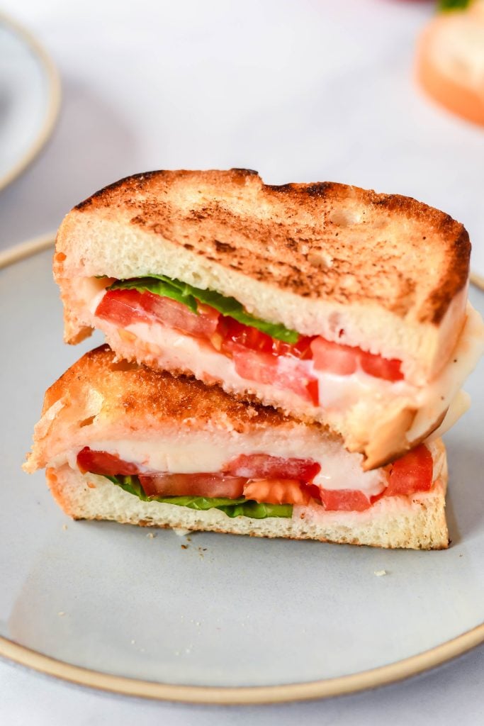 caprese grilled cheese cut in half and shown stacked on a set of gray lunch plates