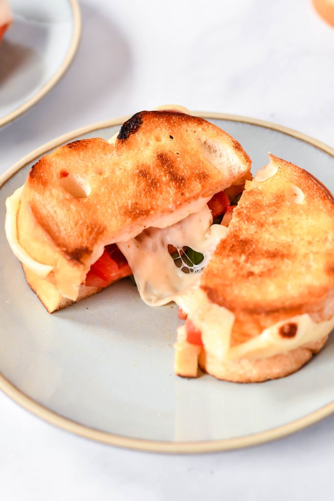 caprese grilled cheese on a stack of gray lunch plates with vine ripened tomatoes in the background