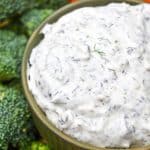 creamy dill dip recipe in a small brown bowl surrounded by an assortment of fresh vegetables and crispy potato chips