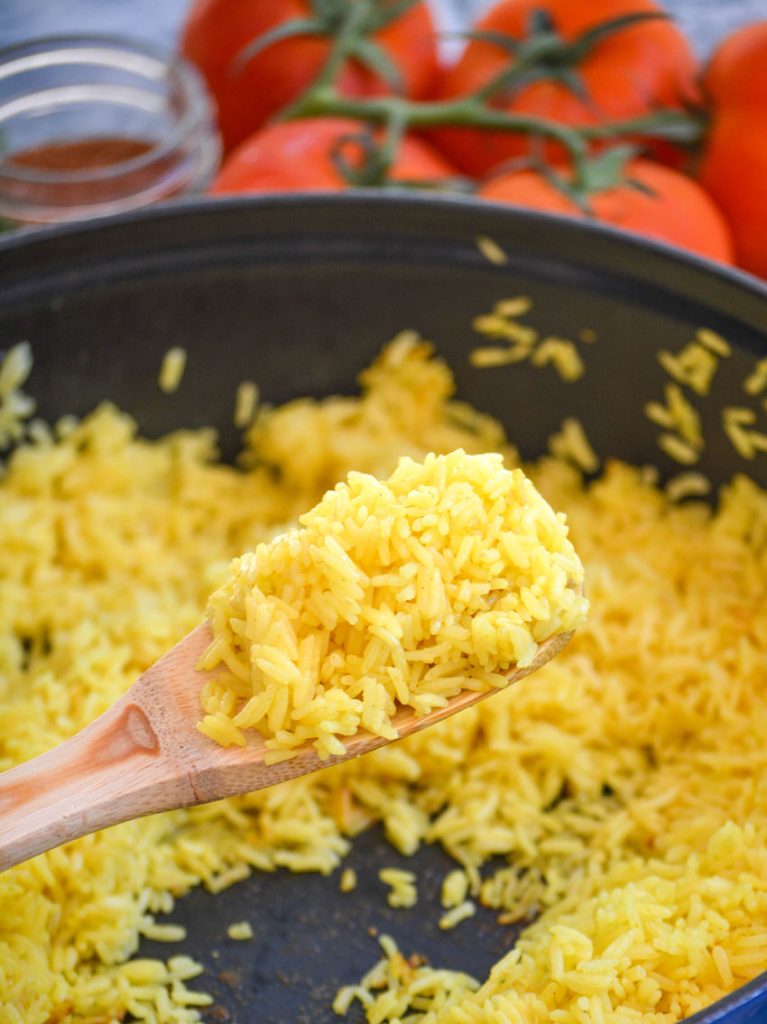 yellow basmati rice held aloft on a wooden spoon with vine ripened tomatoes in the background