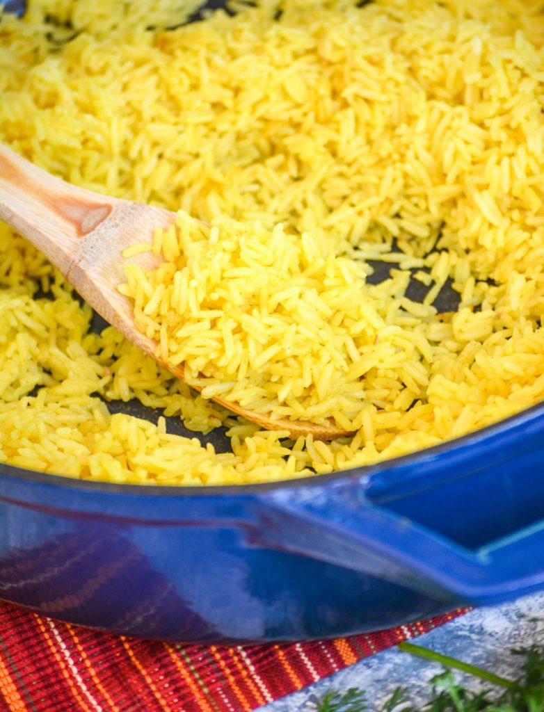 yellow basmati rice scooped on a wooden spoon in a blue enameled cast iron skillet