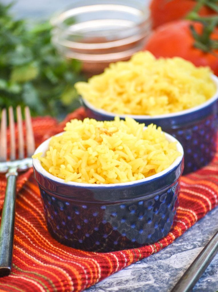 yellow basmati rice in blue ramekins on a cloth napkin with vine ripened tomatoes and fresh cilantro in the background