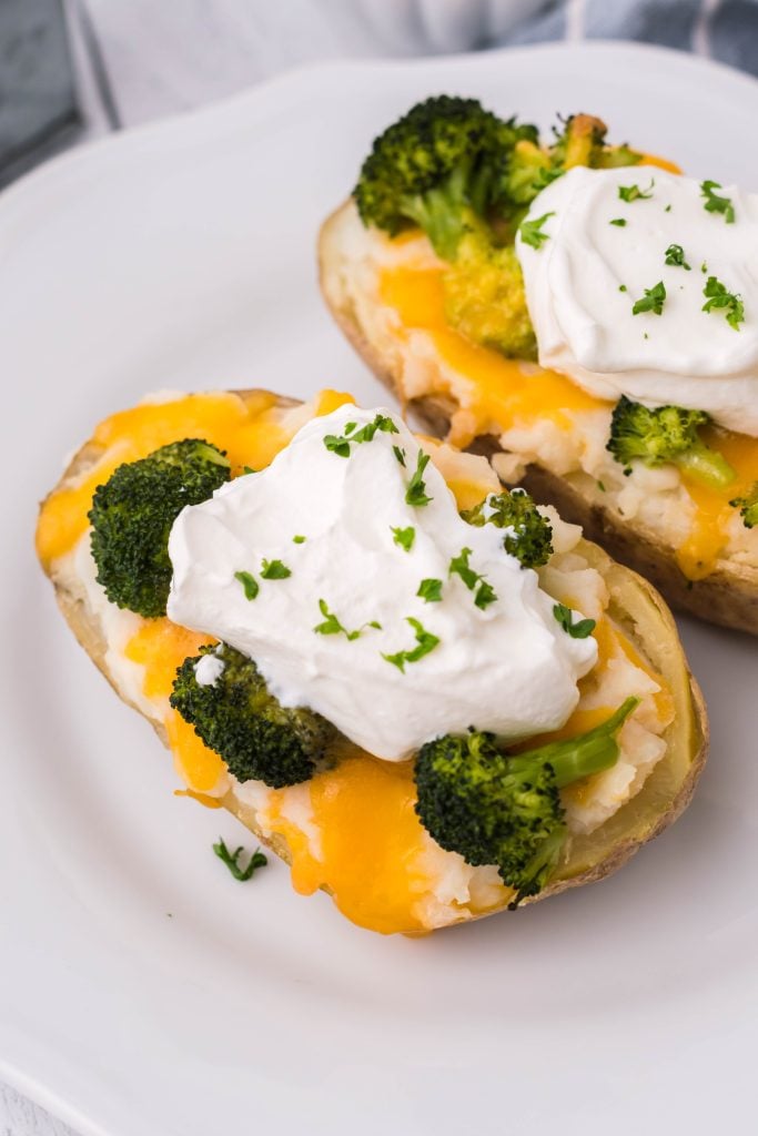 broccoli & cheddar twice baked potatoes topped with a dollop of sour cream and chives served on a white plate