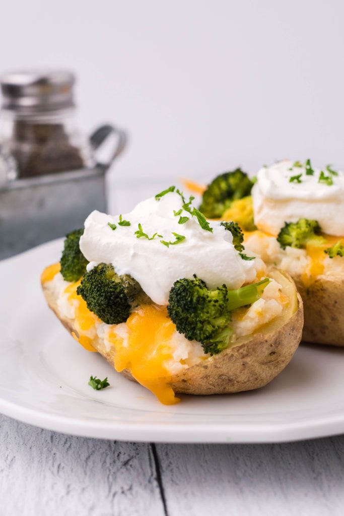 broccoli & cheddar twice baked potatoes topped with a dollop of sour cream and chives served on a white plate