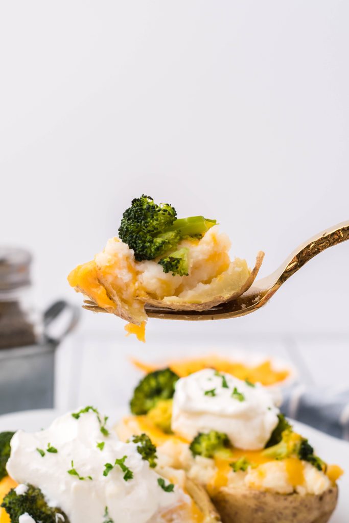 a gold fork holding up a bite of broccoli cheddar twice baked potato