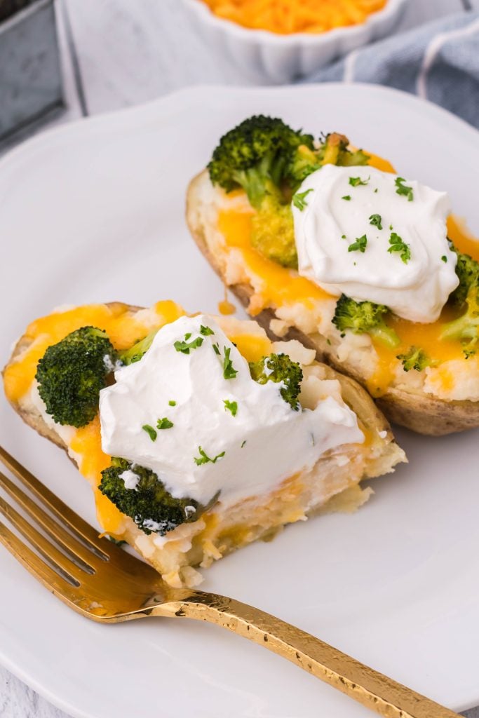 broccoli & cheddar twice baked potatoes topped with a dollop of sour cream and chives served on a white plate