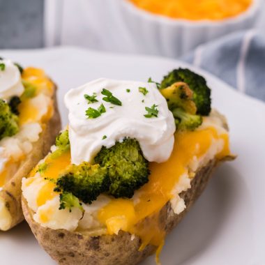 broccoli & cheddar twice baked potatoes topped with a dollop of sour cream and chives served on a white plate