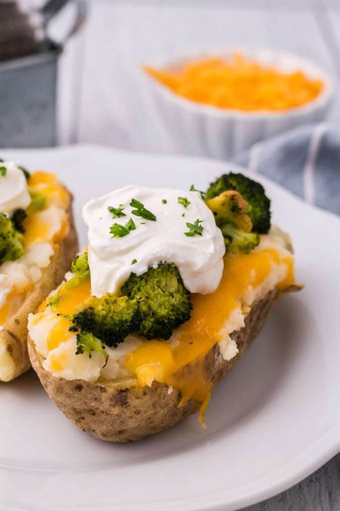 broccoli & cheddar twice baked potatoes topped with a dollop of sour cream and chives served on a white plate