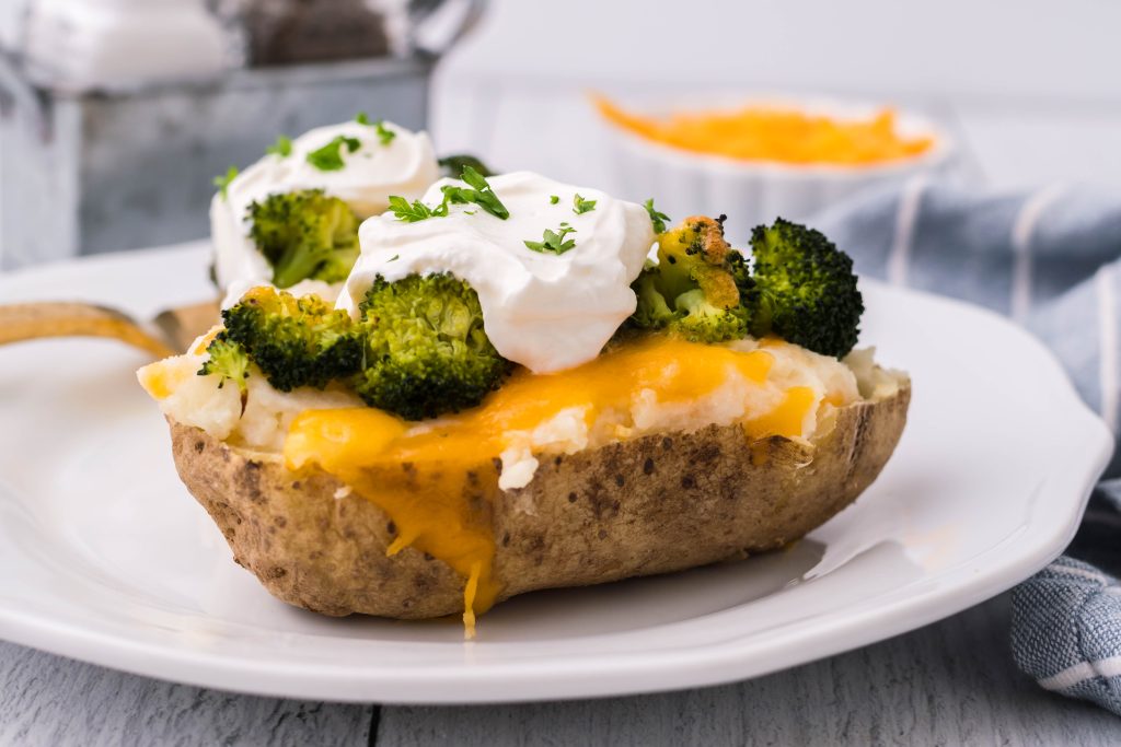 broccoli & cheddar twice baked potatoes topped with a dollop of sour cream and chives served on a white plate