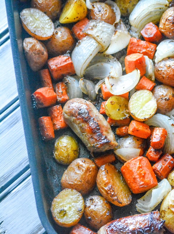 Italian Sausage Potato & Balsamic Vegetable Casserole with carrots shown in a black non-stick roasting pan on a white wooden background