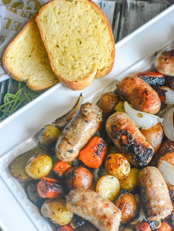 Italian Sausage, Potato, & Balsamic Vegetable Casserole shown on a white platter with garlic bread in the back ground