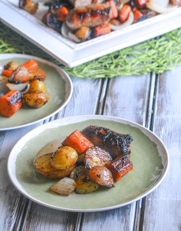 Italian Sausage & Vegetable Sheet Pan Supper shown being served on two white and green serving plates on a white wooden background