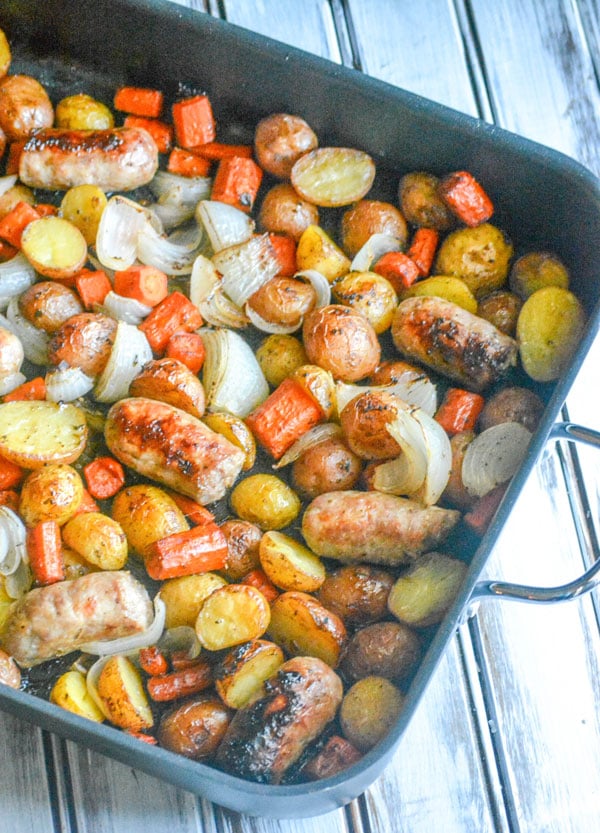 Italian Sausage Potato & Balsamic Vegetable Casserole with carrots shown in a black non-stick roasting pan on a white wooden background