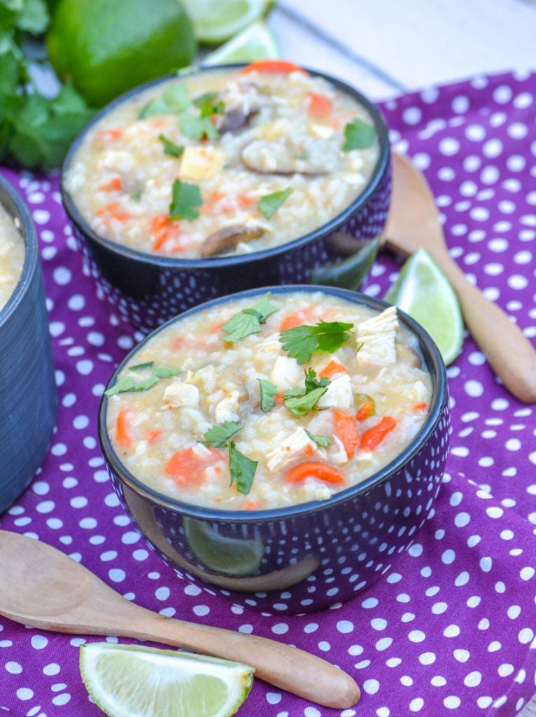 thai chicken coconut soup in a soup pot and shown in two small black bowls, topped with fresh cilantro leaves