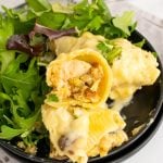 chicken and stuffing stuffed shells on a black plate with leafy greens on the side