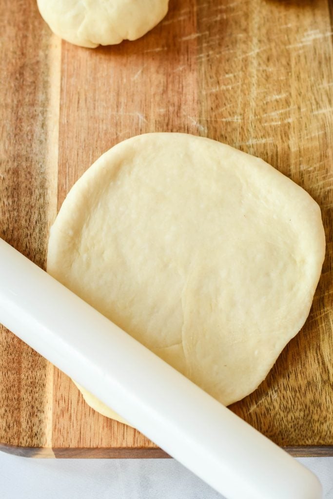 cheeseburger bun dough being rolled out on a wooden cutting board