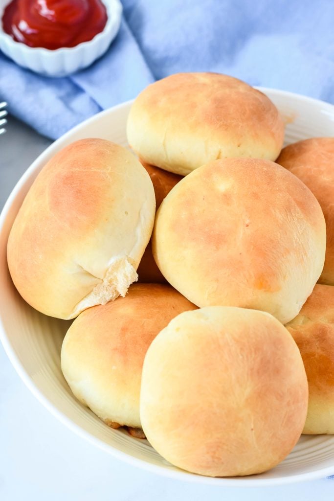 cheeseburger buns piled in a white bowl with ketchup on the side