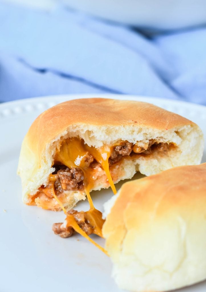 a cheeseburger bun shown on a white plate and pulled apart to reveal the cheesy beef filling inside