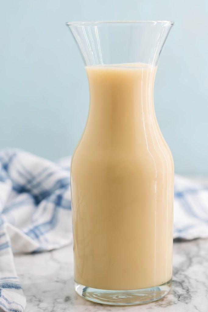 homemade sweetened condensed milk shown in a tall glass jar