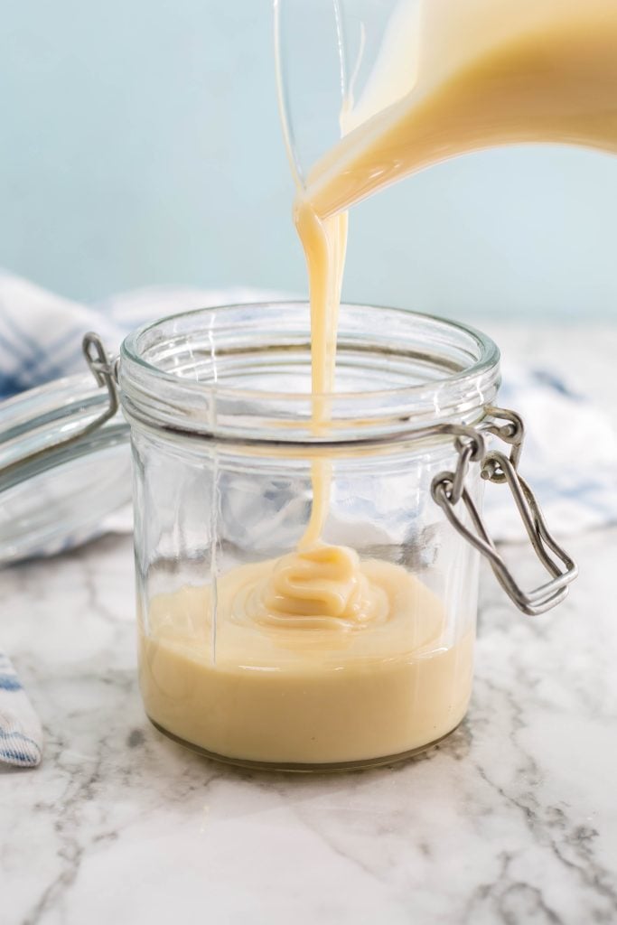 sweetened condensed milk being shown poured into a glass jar with sealable lid for storing