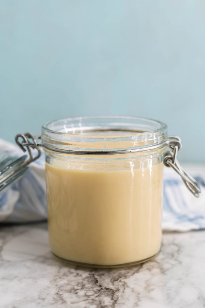 sweetened condensed milk being shown poured into a glass jar with sealable lid for storing