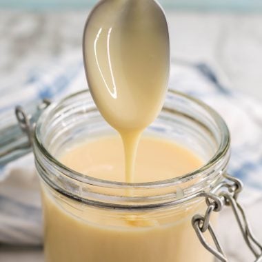 a silver spoon shown with homemade sweetened condensed milk dripping from it into a glass jar