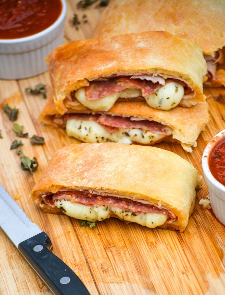 three meat & cheese stromboli shown in slices on a wooden cutting board