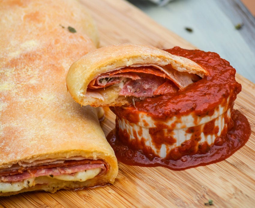 a slice of homemade stromboli shown dipped in a bowl overflowing with marinara sauce