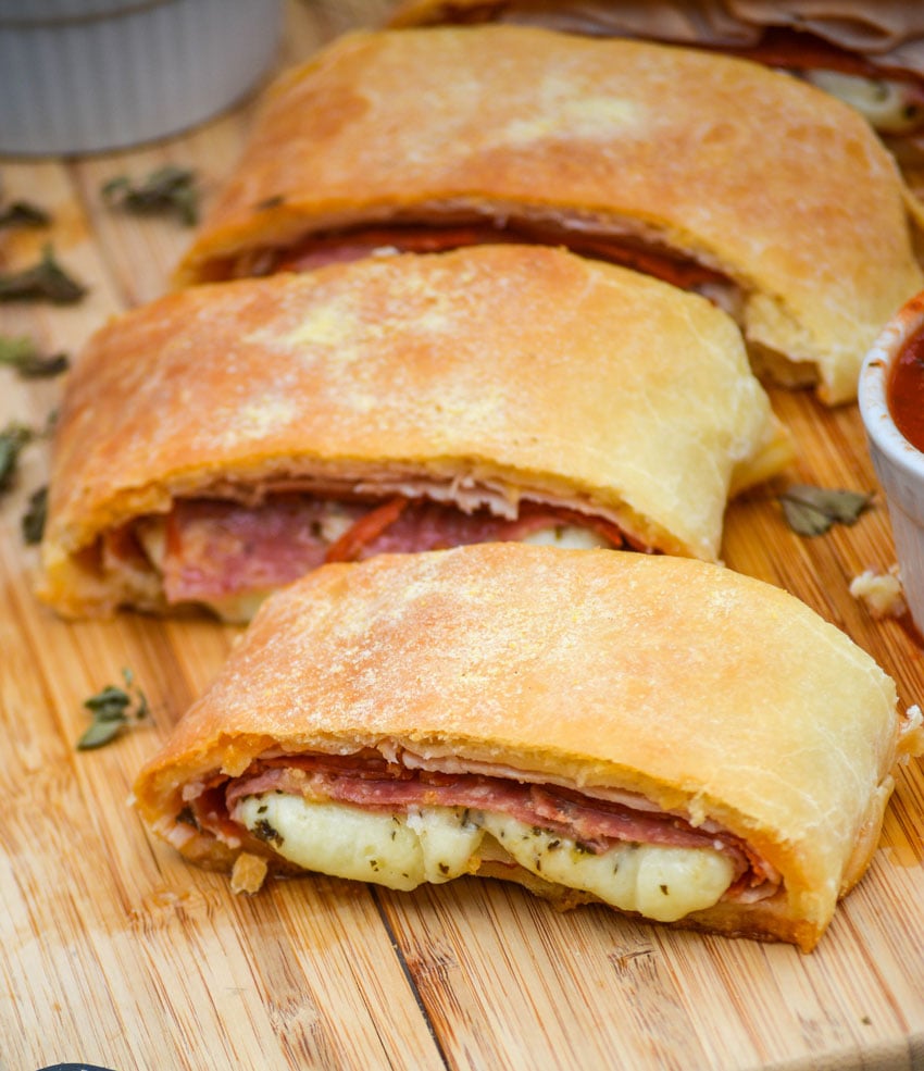 three meat & cheese stromboli shown in slices on a wooden cutting board