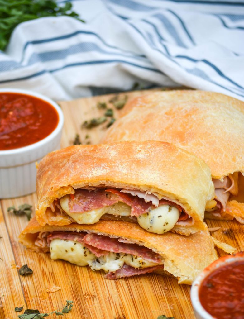 three meat & cheese stromboli shown in slices on a wooden cutting board