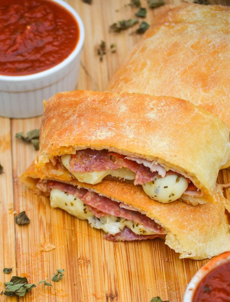 three meat & cheese stromboli shown in slices on a wooden cutting board